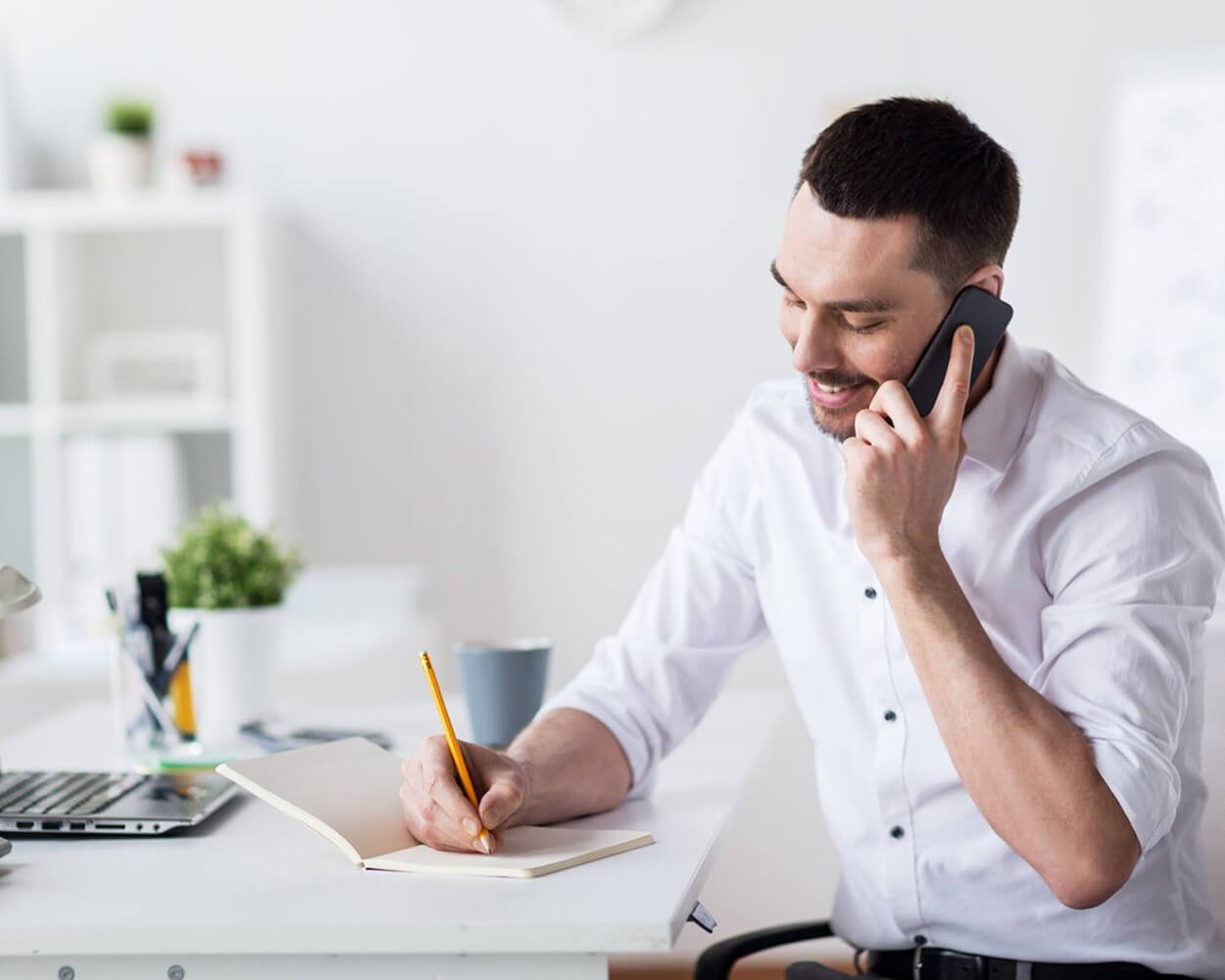 Business man sitting at a desk providing consulting services, talking on the phone and writing down notes.