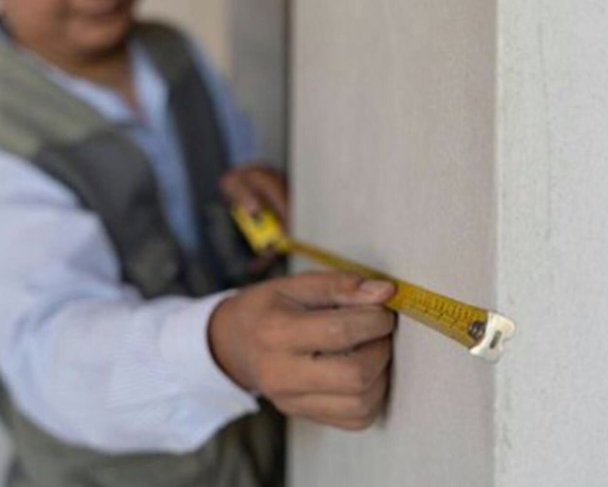 Surveyor or installer using tape measure to measure the width of a building column.